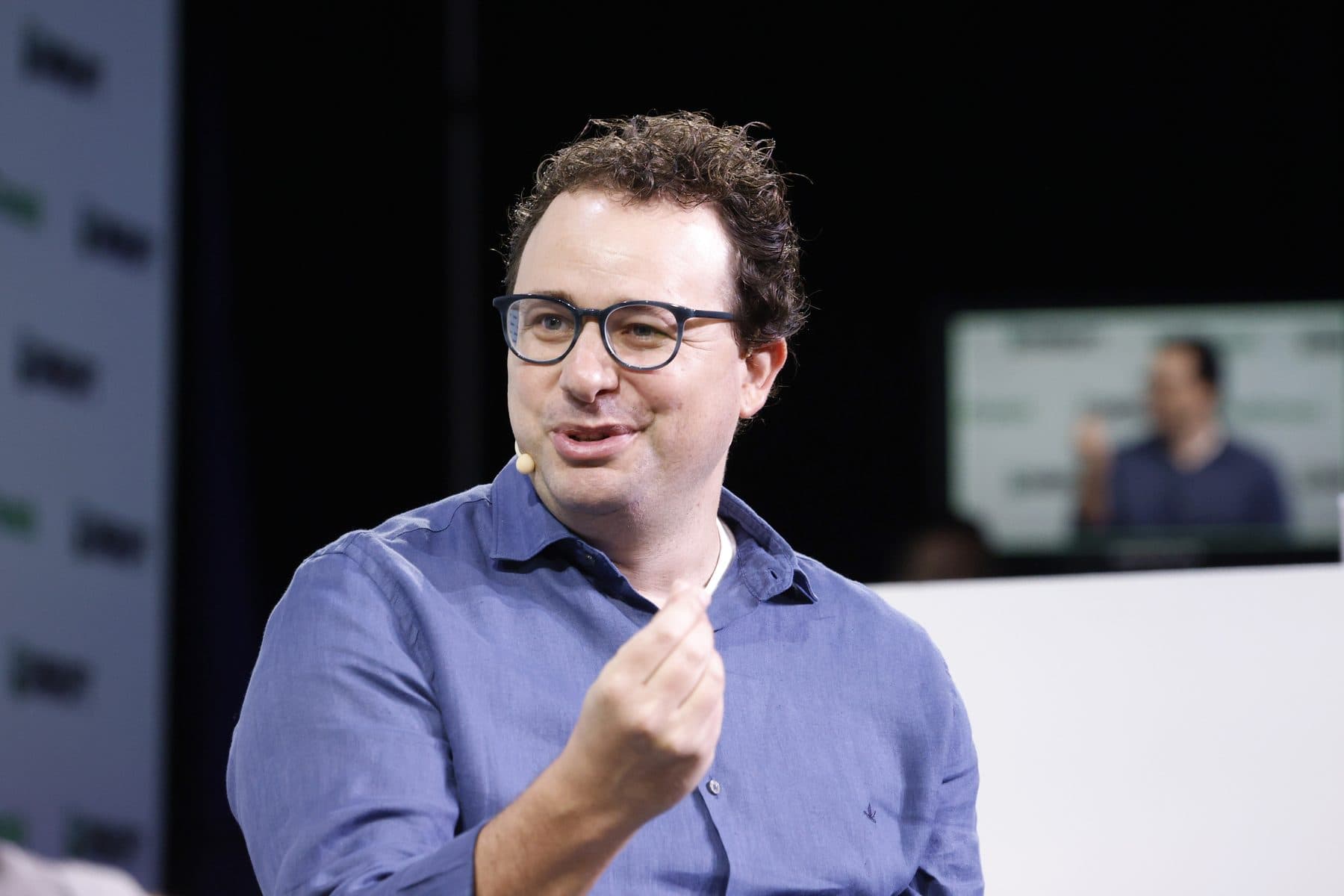 Dario Amodei, cofundador e CEO da Anthropic, de suéter escuro no palco do TechCrunch Disrupt 2023, com microfone e o logotipo do evento ao fundo