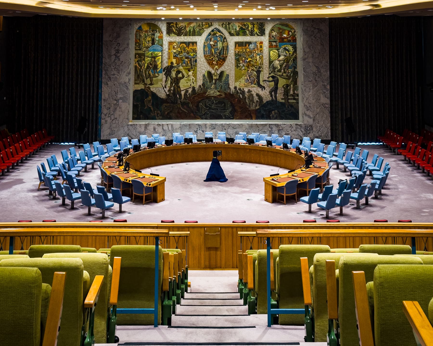 Câmara vazia do Conselho de Segurança da ONU, com a mesa em ferradura e o emblema das Nações Unidas ao fundo