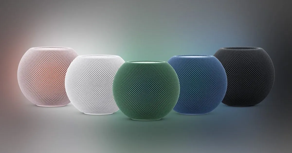 Cinco caixas de som esféricas Apple HomePod mini alinhadas lado a lado nas cores rosa, branca, verde, azul e preta sobre fundo com gradiente