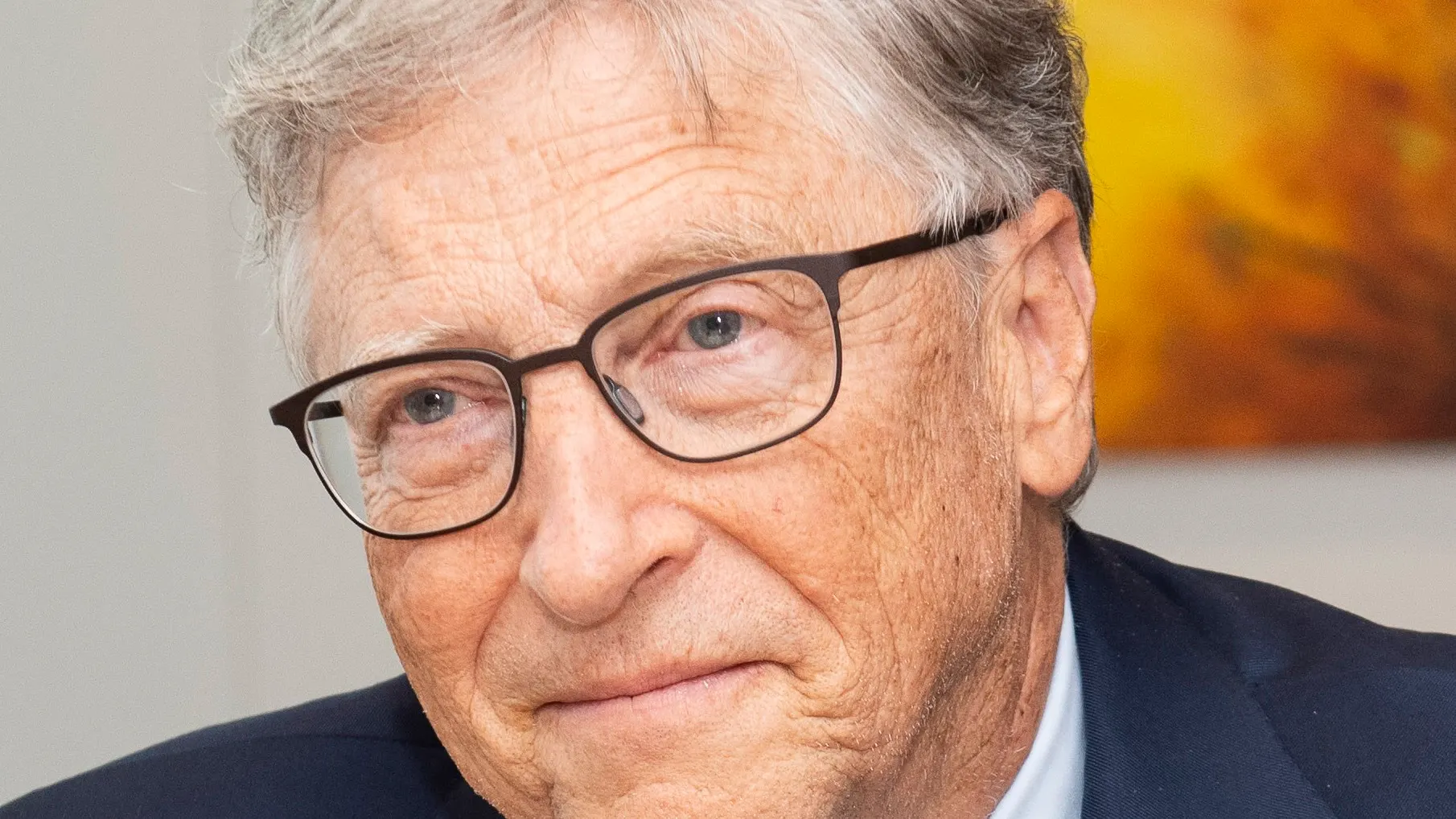 Bill Gates em pé, de suéter azul-marinho com a Fundação Gates no peito, diante de um fundo azul com o logo da Comissão Europeia