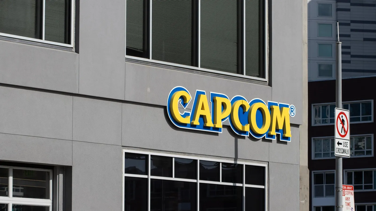 Fachada de predio cinza com o logotipo amarelo e azul da Capcom em destaque acima das janelas