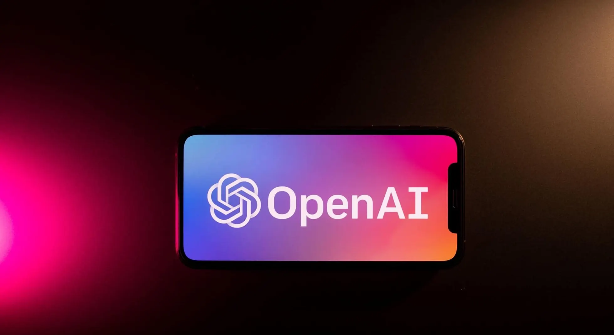 Smartphone posicionado na horizontal exibindo o logotipo da OpenAI em fundo escuro com feixe de iluminação rosa à esquerda