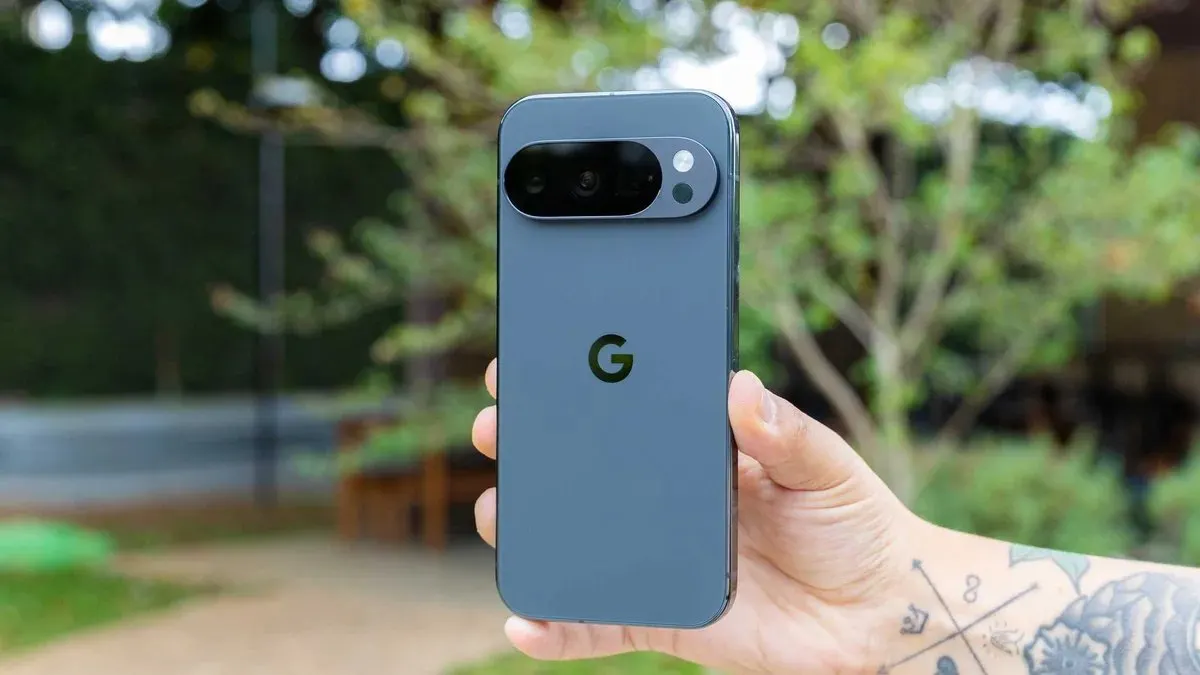 Mão segurando a traseira de um smartphone Google Pixel cinza na vertical, com barra horizontal de câmeras e logotipo da marca contra um jardim desfocado