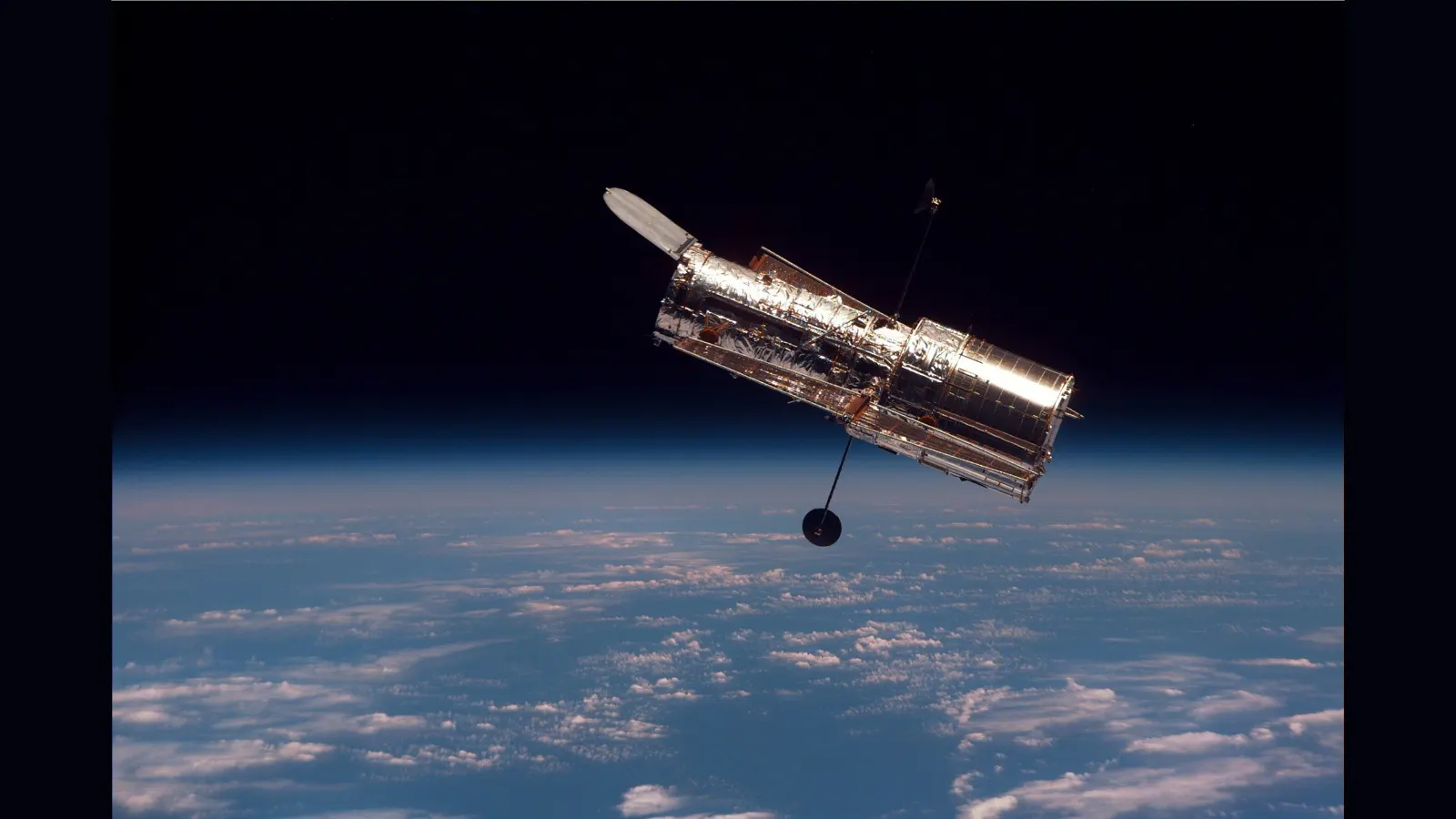 Telescópio cilíndrico prateado acima da Terra com nuvens, antenas estendidas e fundo escuro