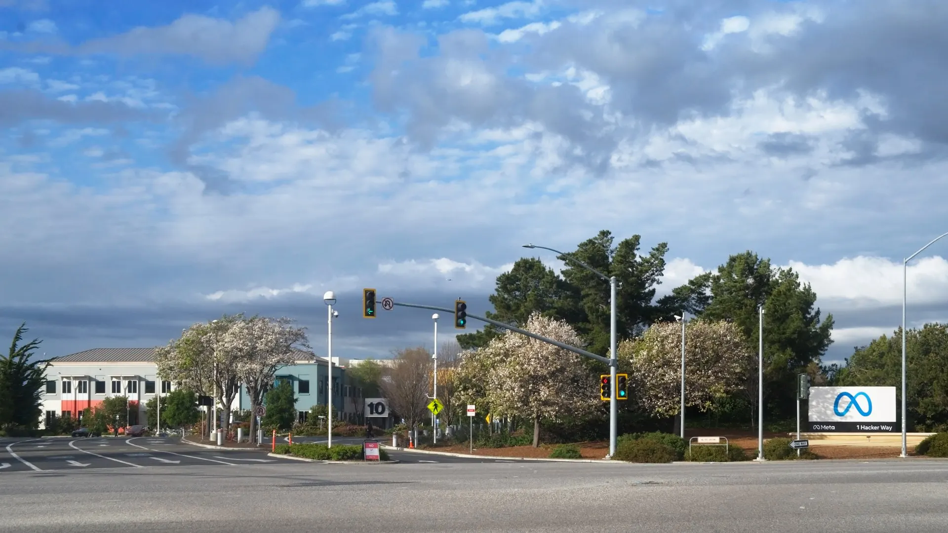 Placa da Meta com o logotipo do infinito, em frente à sede da empresa em Menlo Park, na Califórnia, vista de um cruzamento com árvores floridas
