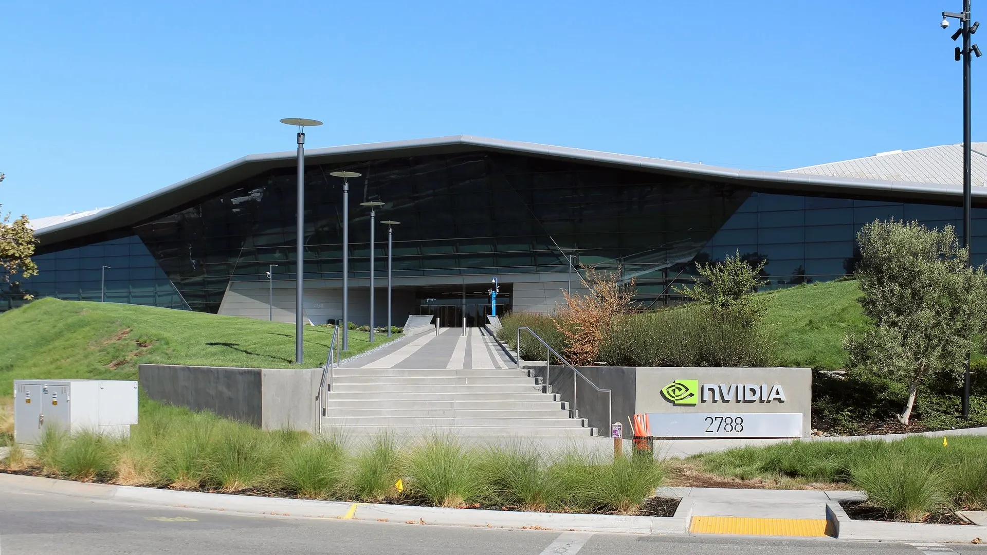 Fachada de vidro do prédio da Nvidia em Santa Clara, na Califórnia, com escada de concreto, gramado e o logotipo da empresa na entrada