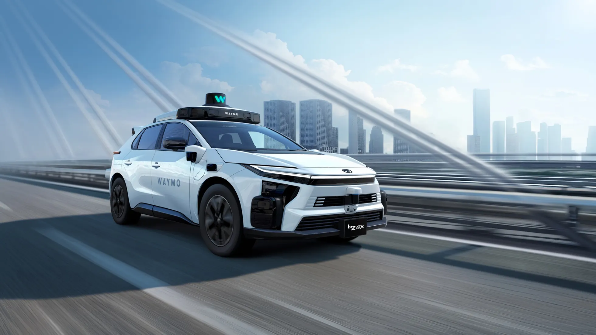 SUV branco com inscrições Waymo, equipamentos sobre o teto e na dianteira, em uma ponte com prédios ao fundo