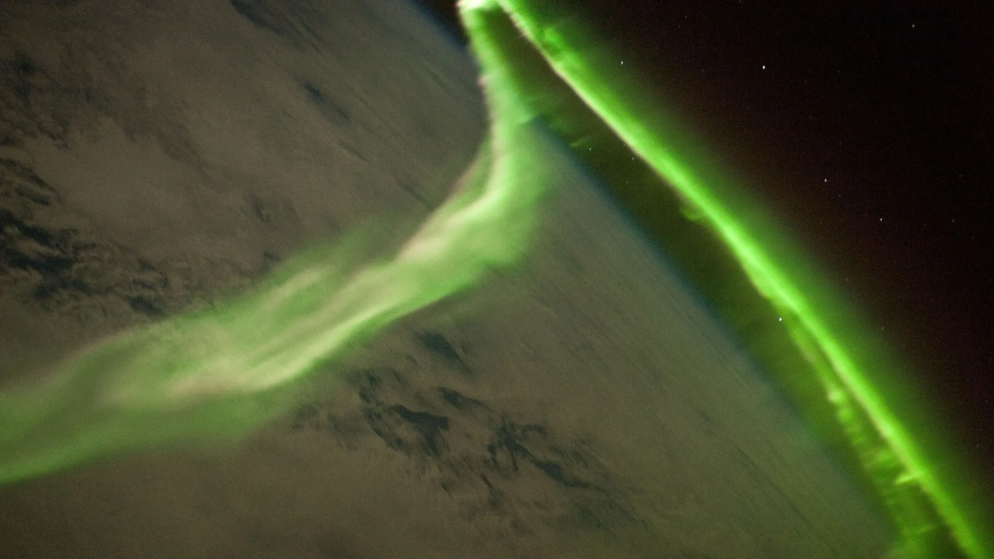 Faixas luminosas verdes sobre nuvens e a curvatura da Terra, com fundo escuro e pequenos pontos de luz
