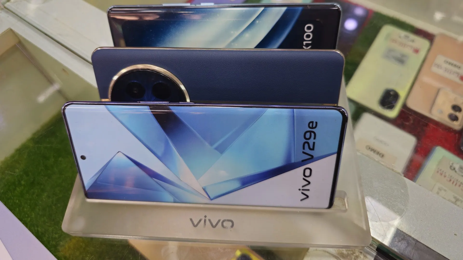 Três celulares da Vivo em um suporte de vitrine, com o modelo V29e à frente e o logotipo da marca na base; imagem ilustrativa, não é o Y600