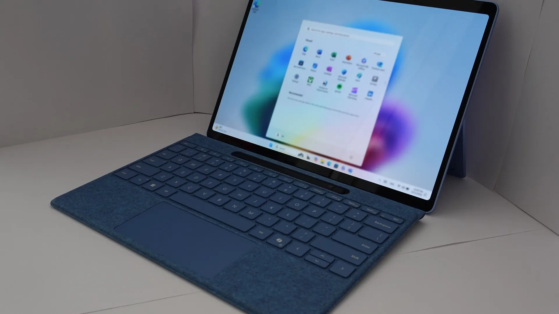 Notebook 2 em 1 azul com a tela mostrando o menu Iniciar do Windows 11, sobre fundo cinza. Foto ilustrativa, não é material do lançamento