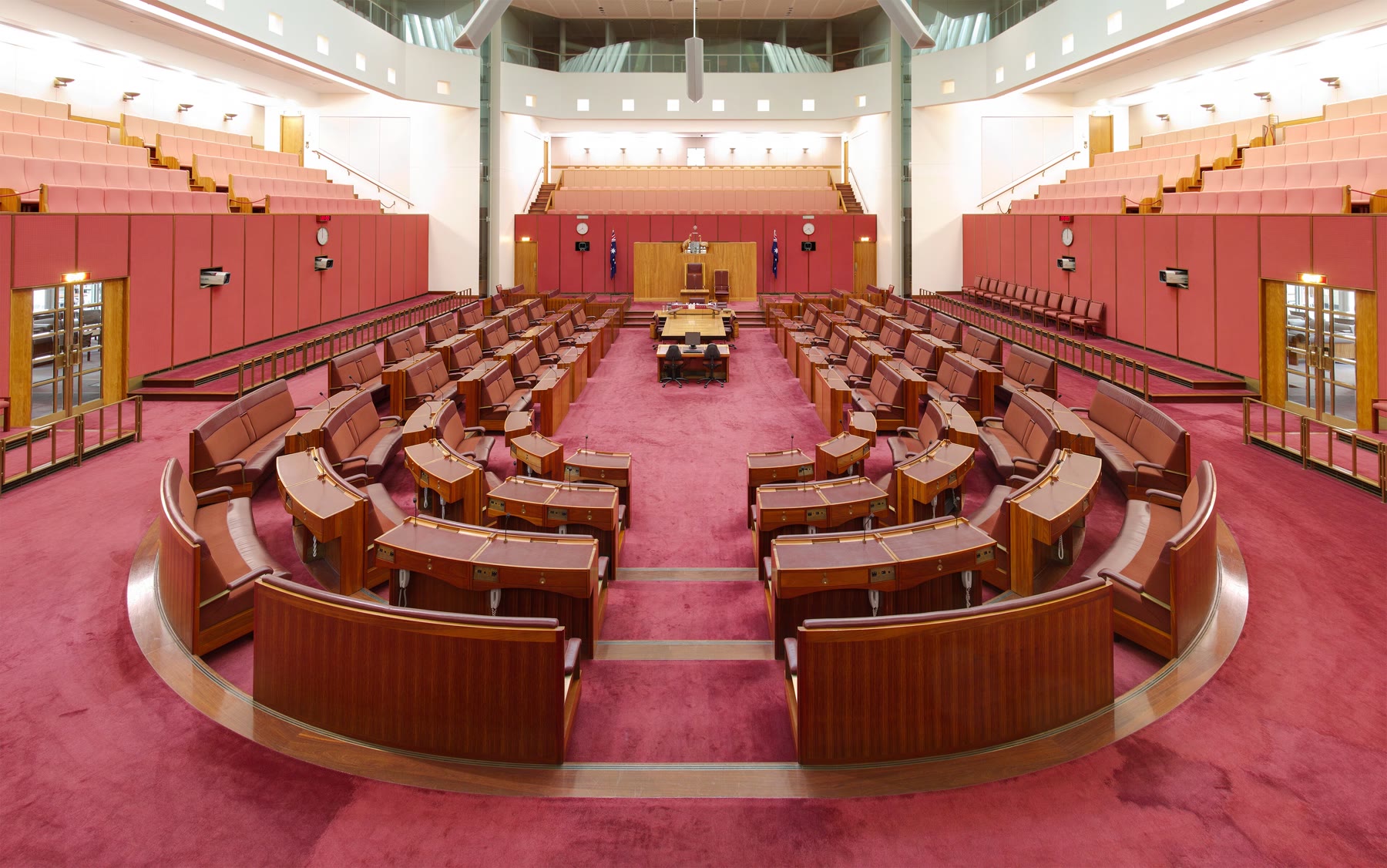 Plenário vazio do Senado australiano, com bancadas vermelhas em ferradura, a mesa central de madeira e as galerias acima