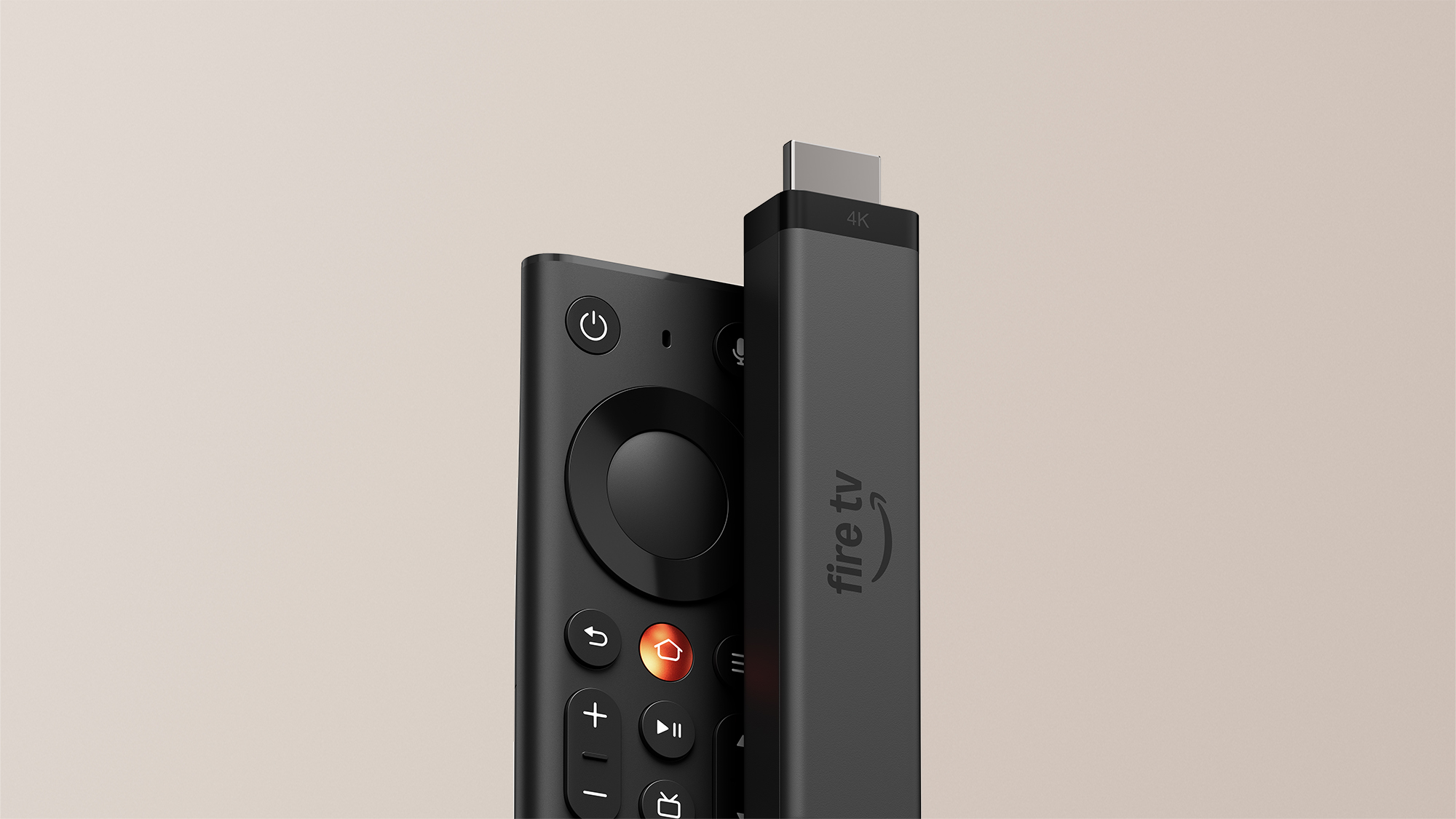 Dongle Fire TV Stick 4K em pé com conector HDMI visível no topo e logotipo fire tv na lateral fosca escura, apoiado ao lado do novo controle remoto Fire TV preto com botão Home metálico em tom cobre avermelhado, direcional circular e botões em relevo sobre fundo bege claro