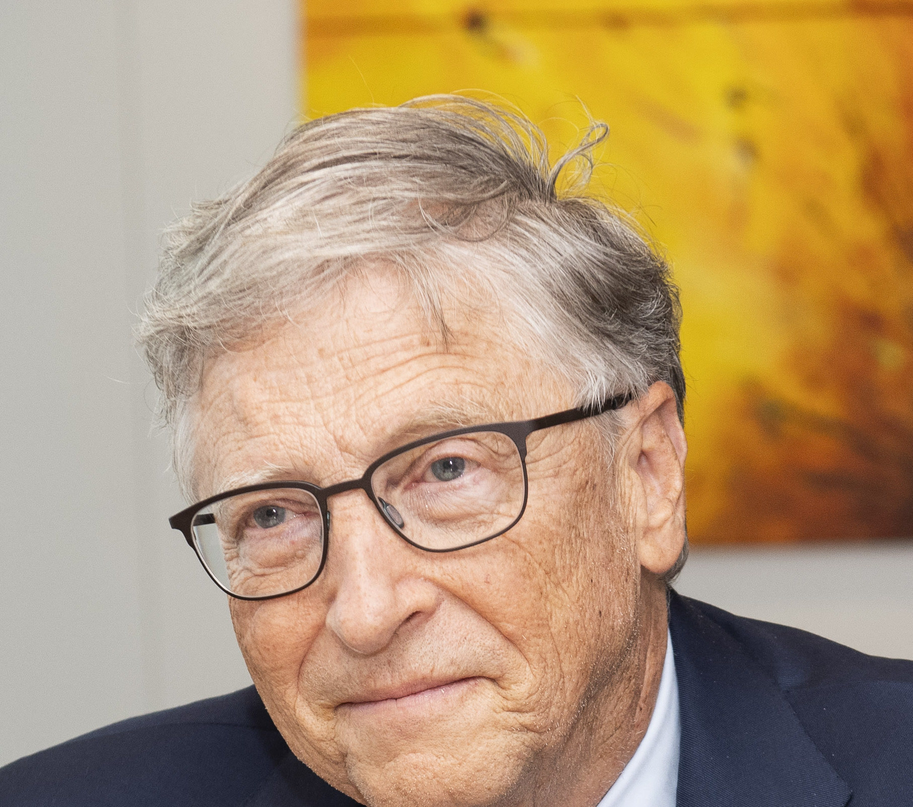 Bill Gates de suéter azul-marinho, com as mãos na frente do corpo, diante do fundo azul da Comissão Europeia