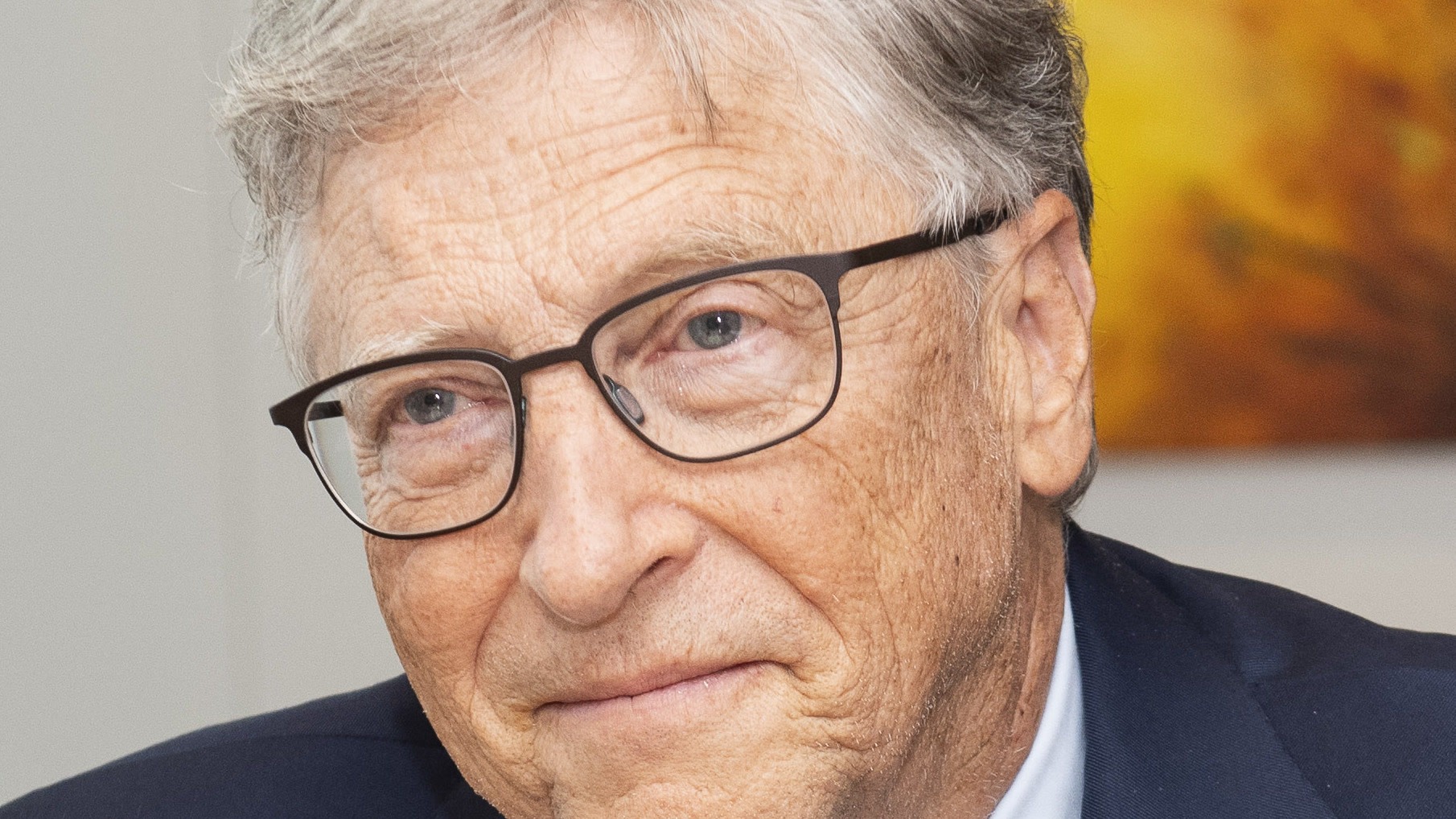 Bill Gates em pé, de suéter azul-marinho com a Fundação Gates no peito, diante de um fundo azul com o logo da Comissão Europeia