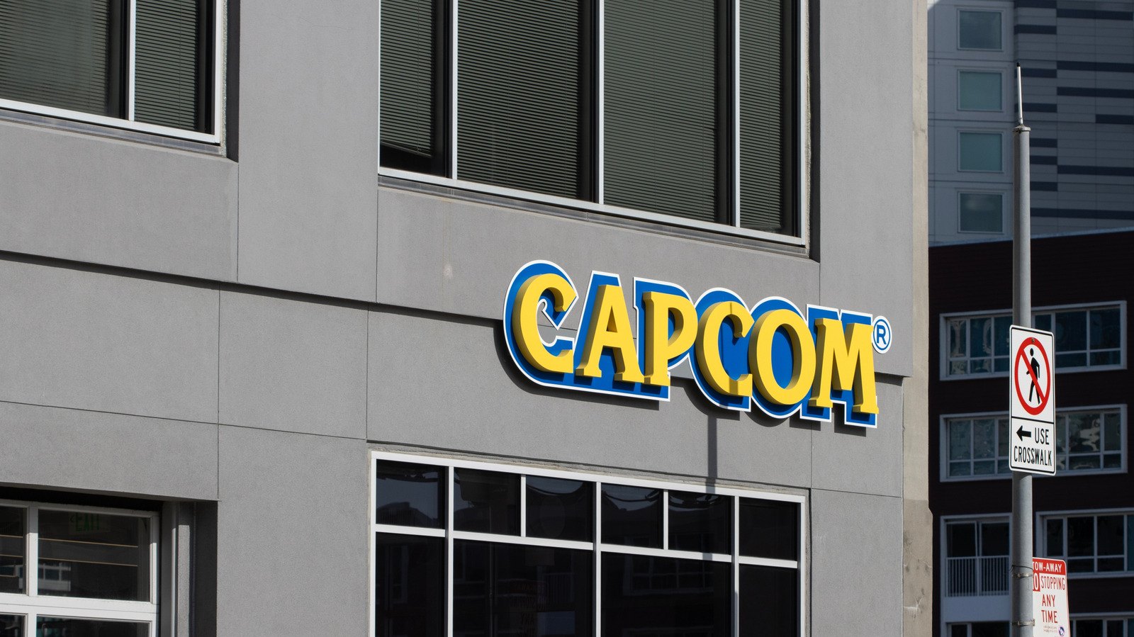 Fachada externa de um prédio corporativo de concreto cinza com o logotipo em relevo amarelo e azul da Capcom sobre janelas espelhadas