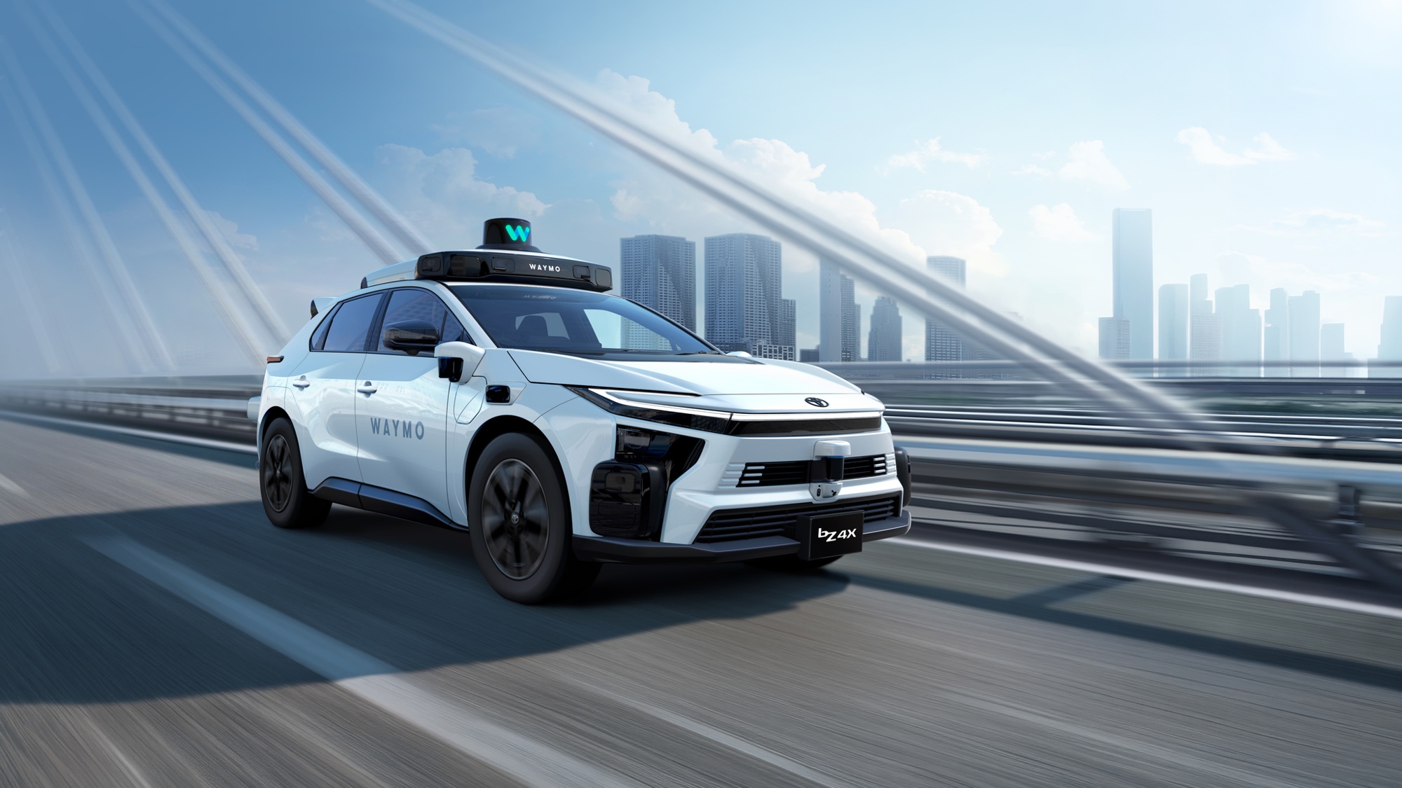 SUV branco com inscrições Waymo, equipamentos sobre o teto e na dianteira, em uma ponte com prédios ao fundo